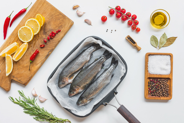 view from above of fish in baking tray surrounded by various ingredients on white table - Φωτογραφία, εικόνα