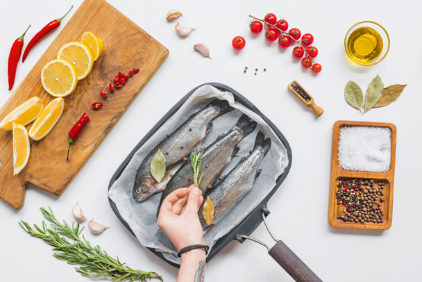 cropped image of woman decorating fish in tray with baking paper by rosemary on table with ingredients - Foto, imagen