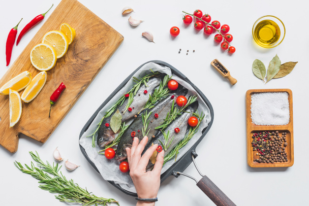 partial view of woman decorating fish in tray with baking paper by cherry tomatoes on table with ingredients - Valokuva, kuva
