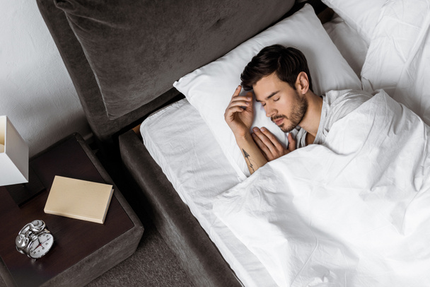 bovenaanzicht van knappe bebaarde jonge man slapen in bed in de ochtend - Foto, afbeelding
