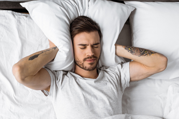 fiatal férfi záró füle párna az ágyban reggel - Fotó, kép
