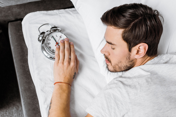 top view of young man holding alarm clock and sleeping in bed - Photo, Image