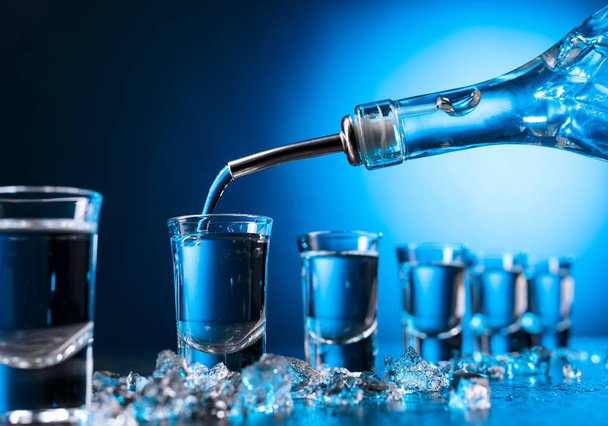 Vodka vertido en un vidrio iluminado con luz de fondo azul. Copiar espacio.Vodka refrigerado con trozos de hielo
. - Foto, imagen