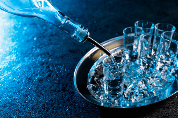 Vodka versé dans un verre éclairé avec rétro-éclairage bleu.Vodka réfrigérée avec des morceaux de glace
. - Photo, image