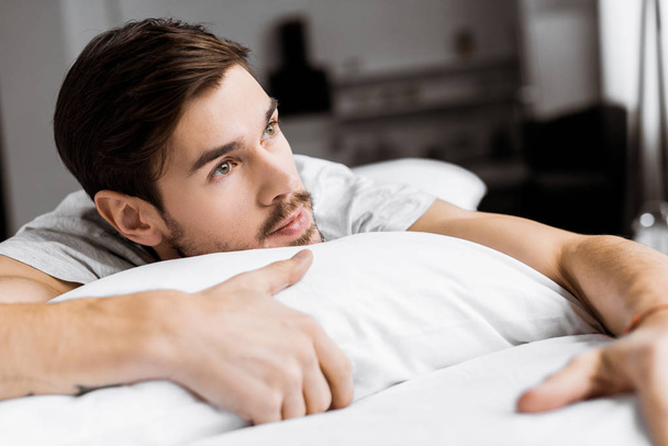 pensive young man lying on bed and looking away in the morning - Foto, Imagem