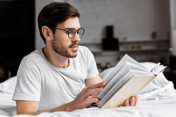 giovane uomo con gli occhiali sdraiato a letto e leggere libro al mattino
 - Foto, immagini