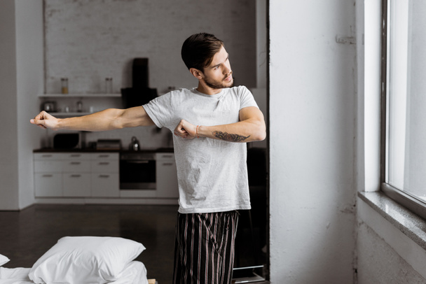jonge man in pyjama uit te oefenen en venster kijken in de ochtend - Foto, afbeelding
