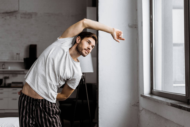 handsome young man in pajamas exercising and looking at window in the morning - Foto, Bild