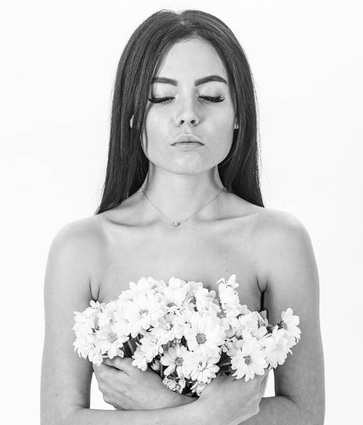 Skin care concept. Girl on calm face stands naked and holds chamomile flowers in front of chest. Woman with smooth healthy skin looks attractive. Lady covers breasts with flowers, isolated on white - Photo, Image