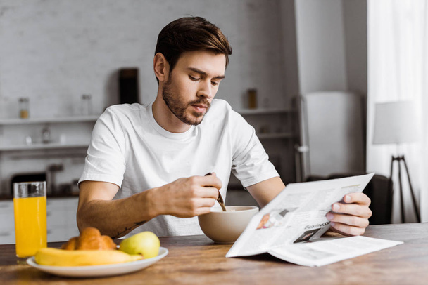 handsome young man having breakfast and reading newspaper at home - Photo, Image