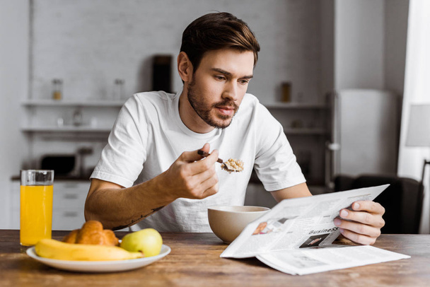 komea nuori mies syö muroja aamiaiseksi ja lukee sanomalehteä kotona
 - Valokuva, kuva