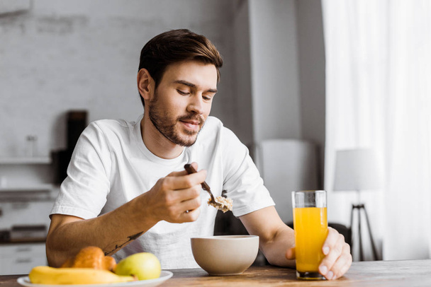 joven guapo tomando cereal con jugo de naranja en casa
 - Foto, Imagen