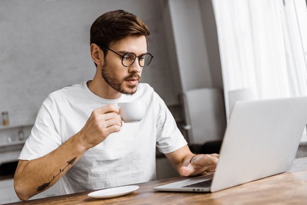 confident young freelancer with coffee working with laptop at home - Photo, Image