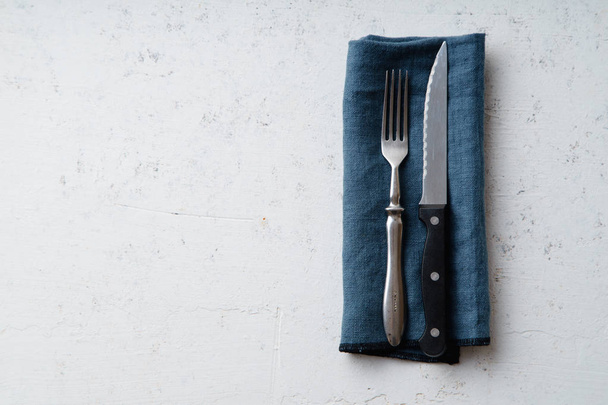 Knife and fork on blue textile napkin on concrete stone background with copy space - Fotoğraf, Görsel