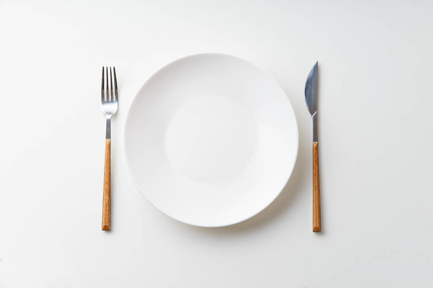 White empty plate with knife and fork isolated on white background, top view   - Fotografie, Obrázek
