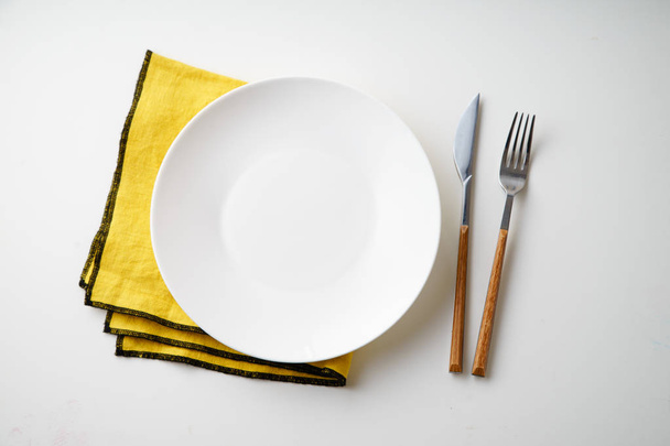 White empty plate with knife and fork and yellow textile napkin isolated on white background, close-up  - Zdjęcie, obraz
