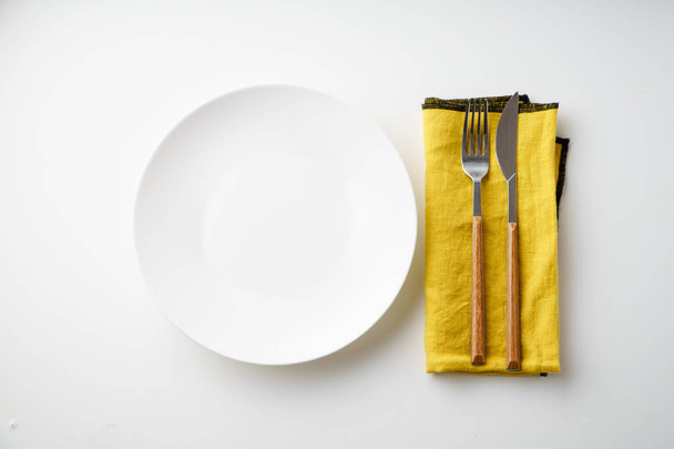 Beyaz boş plaka bıçak ve çatal ve beyaz arka plan üzerinde izole sarı Tekstil peçete ile yakın çekim  - Fotoğraf, Görsel