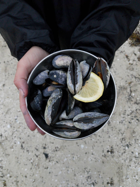 Photo of hands of man holding iron cup with mussels - 写真・画像