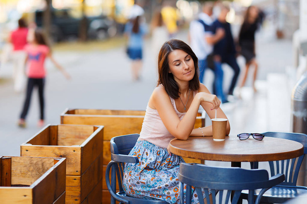 Porträt einer schönen lächelnden, glücklichen Dame bei einem heißen Kaffee, die auf einer Sommerterrasse in einem Café sitzt. ein junges Mädchen sitzt an einem Restauranttisch und trinkt Kaffee. - Foto, Bild
