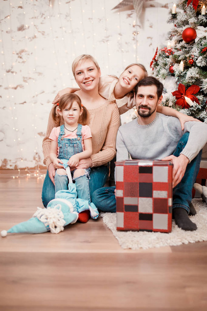 Photo of happy family sitting with box with gift at decorated New Year tree - Valokuva, kuva