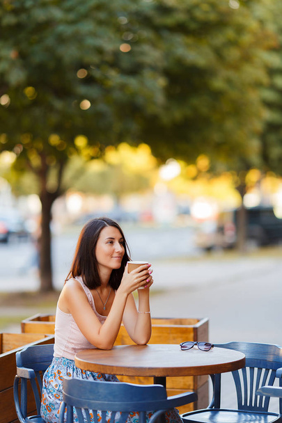 Portrét krásné usměvavé Happy lady s horkou kávou, posezení na letní terase v Cafe. Mladá dívka sedí a pití kávy v restauraci stůl. - Fotografie, Obrázek