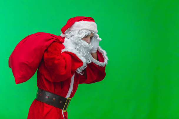 Boże Narodzenie. Rodzaju i zmęczony Święty Mikołaj w białe rękawiczki niesie ze sobą czerwony worek z prezenty, na ramieniu. Na białym tle na zielonym tle - Zdjęcie, obraz