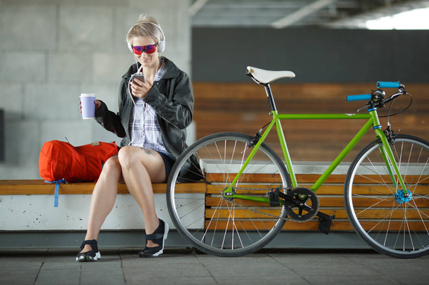 Image of young woman with glass sitting on bench next to green bicycle - Foto, Imagen