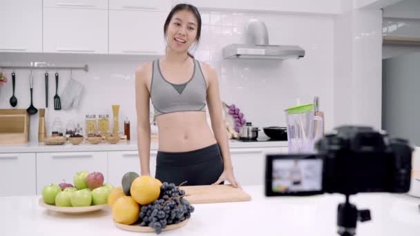 Blogger sportivo donna asiatica utilizzando fotocamera registrazione come fare video succo d'uva per il suo abbonato, femminile utilizzare frutta biologica facendo succo d'uva da sola a casa. Concetto di cibo sano
. - Filmati, video