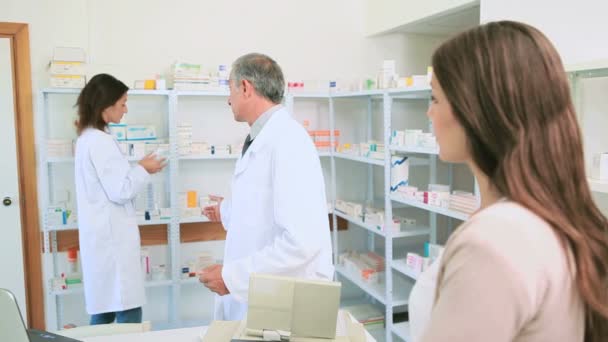 Smiling pharmacist talking to a colleague in front of a female client - Кадри, відео