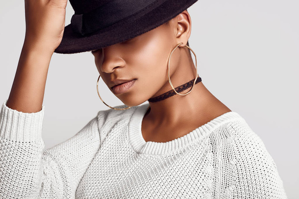 Close-up portret van jonge mooie hipster zwart meisje in de witte trui en mode hoed geïsoleerd op een witte achtergrond. Studio shoot. - Foto, afbeelding