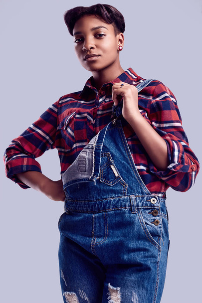 Sensual portrait of glamor elegant black hipster girl with short hair in a plaid shirt and denim overalls posing on colorful background in studio - Φωτογραφία, εικόνα