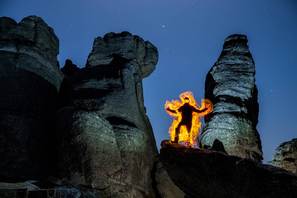 hombre en llamas fotografiado con técnica de pintura ligera sobre una formación rocosa
 - Foto, Imagen