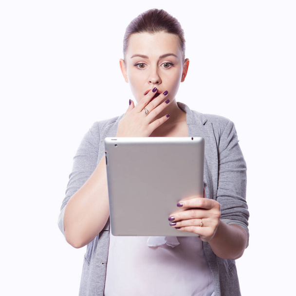 Γυναίκα μελαχρινή συν μέγεθος σε smart casual ντύσιμο (jacker και μπλούζα) σε ένα απομονωμένο άσπρο φόντο. Κατέχει gadgets στα χέρια ger: tablet και τηλέφωνο. Ανεξάρτητος επιχειρηματική ιδέα: εργασία στο διαδίκτυο, Smm - Φωτογραφία, εικόνα