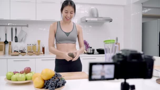 Blogger sporty Asian woman using camera recording how to make avocado juice video for her subscriber, female use organic fruit making avocado juice by herself at home. Healthy food concept. - Footage, Video