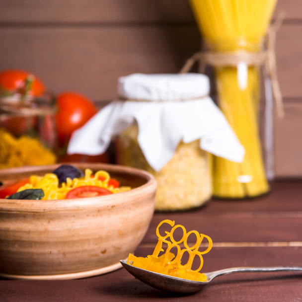 gutes Essen wird mit Nudeln auf einem Löffel in der Nähe eines Tellers mit Fertignudeln mit Tomaten, Basilikum und Parmesan auf einem ländlichen Holztisch ausgelegt. gesundes veganes Ernährungskonzept - Foto, Bild