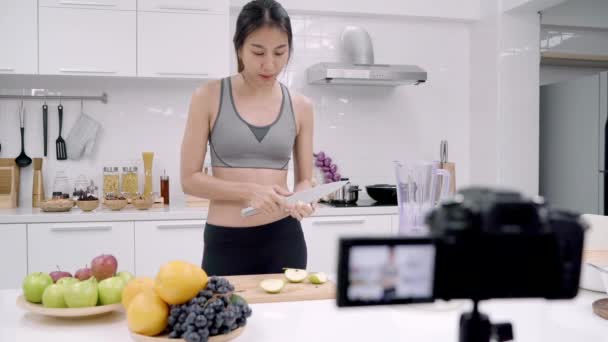 Blogger sporty Asian woman using camera recording how to make apple juice video for her subscriber, female use organic fruit making apple juice by herself at home. Healthy food concept. - Footage, Video