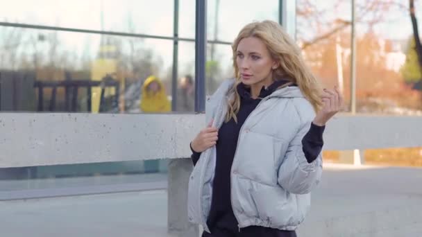 Attractive woman walking down the city street in a down jacket. Urban lifestyle. - Filmagem, Vídeo
