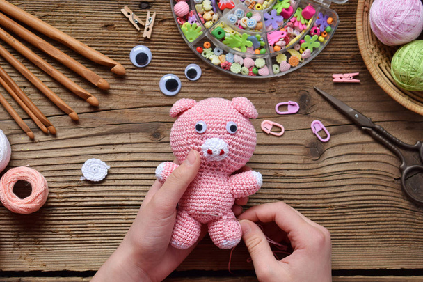 Making pink pig. Crochet toy for child. On table threads, needles, hook, cotton yarn. Step 2 - to sew all details of toy. Handmade crafts. DIY concept. Small business. Income from hobby. - Photo, Image