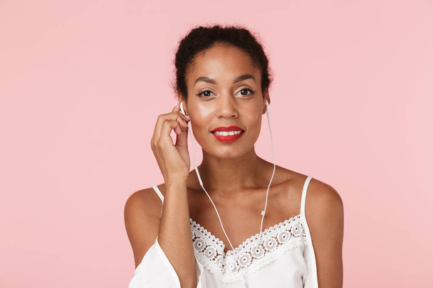 Image of young happy beautiful woman posing isolated over pink background listening music by earphones. - Photo, Image
