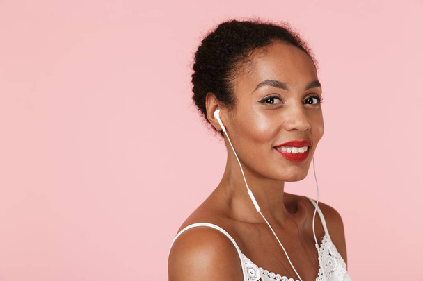 Image of pretty young woman posing isolated over pink wall background listening music with earphones. - Foto, Imagem