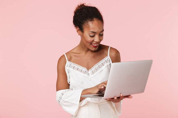 Image of pretty young woman posing isolated over pink wall background using laptop computer. - Fotó, kép