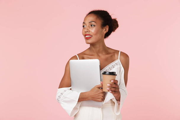 Image of pretty young woman posing isolated over pink wall background looking aside drinking coffee holding laptop computer. - Foto, immagini