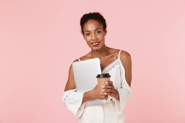 Image of pretty young woman posing isolated over pink wall background drinking coffee holding laptop computer. - Zdjęcie, obraz