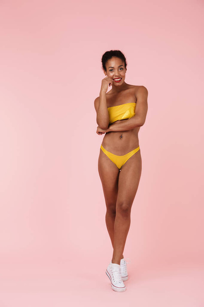 Image of beautiful young woman in swimwear posing isolated over pink wall background. - 写真・画像