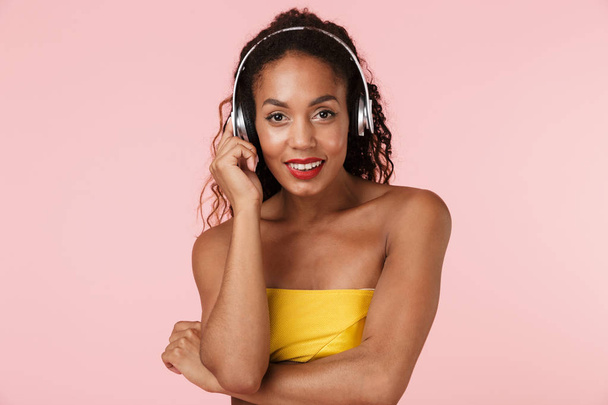 Image of young cheerful woman in swimwear posing isolated over pink background listening music with headphones. - Photo, Image
