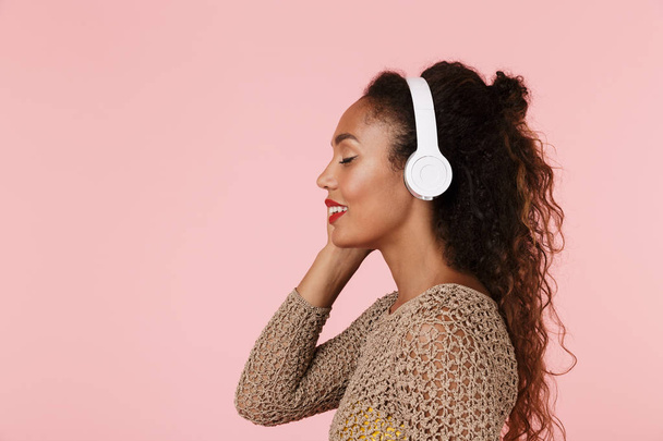 Image of young beautiful woman posing isolated over pink background listening music with headphones. - Foto, imagen