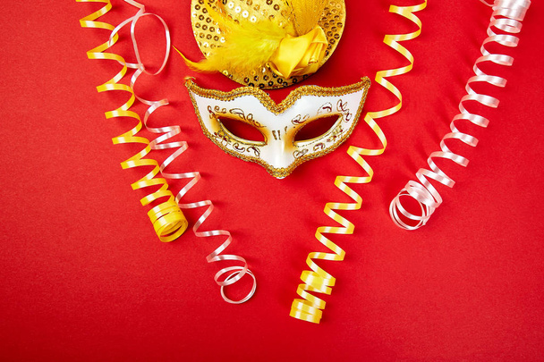 Yellow and white carnival mask on red background. Top view image of masquerade background. Flat lay. Mardi Gras celebration concept. Copy space. - Photo, Image