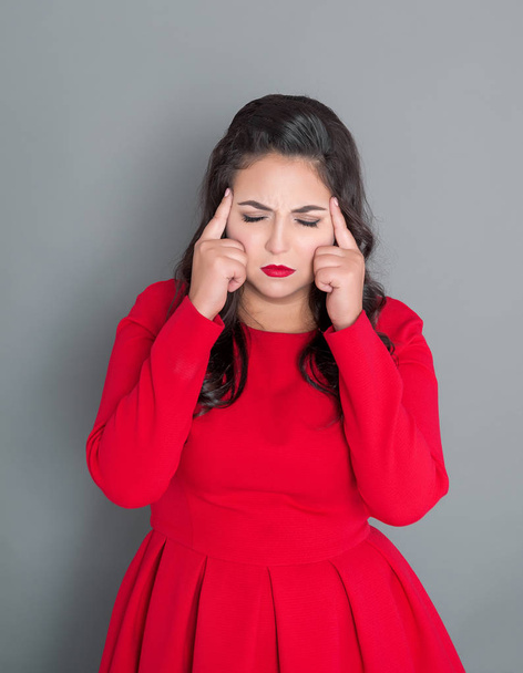 Plus size woman in red dress with headache on gray background - Foto, Imagem