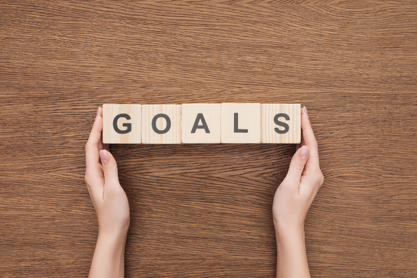 partial view of person holding 'goals' word made of wooden blocks on wooden tabletop, goal setting concept - Foto, imagen