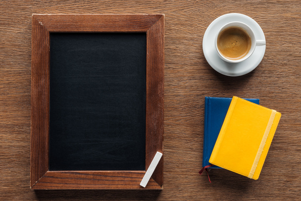 Top view of chalk board with notebooks and coffee on wooden background - Foto, imagen